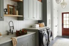 a farmhouse mudroom laundry wiht white shiplap walls, slate grey shaker cabinets, stained shelves and baskets for storage