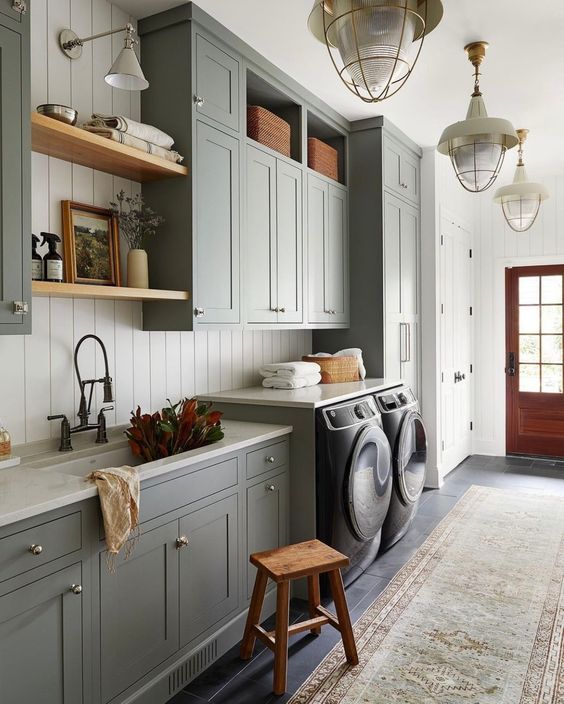 a farmhouse mudroom laundry wiht white shiplap walls, slate grey shaker cabinets, stained shelves and baskets for storage