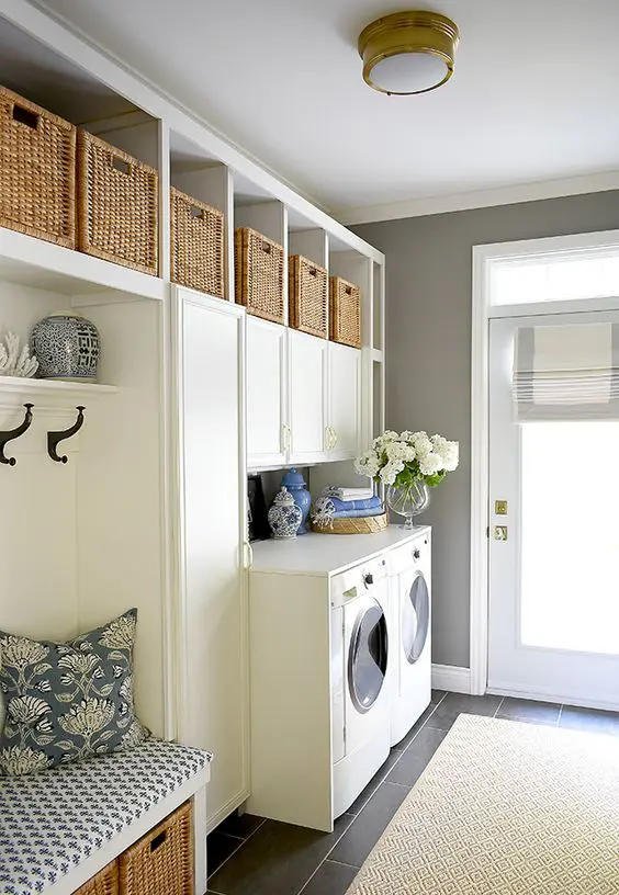 a farmhouse mudroom laundry with shaker cabinets, wicker baskets, a bench with storage and some appliances