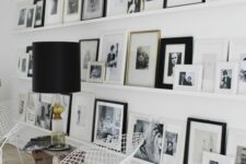 a floor to ceiling gallery wall with black and white artwork, white metal chairs, a wooden bench and a cool lamp