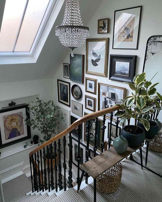a gallery wall from floor to ceiling that takes a staircase wall, a crystal chandelier and some greenery on the bench for a wow look