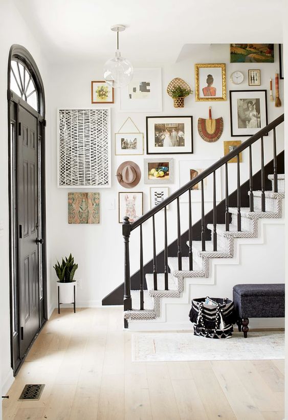 a gorgeous entryway with a colorful gallery wall over the stairs, with not only artwork and photos but also hats, greenery and fans