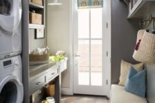 a grey farmhouse mudroom laundry with shaker cabinets and an open storage unit, an upholstered bench, a washing machine and a dryer