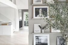 a grey wall with matching ledges, black and white artworks in light colored frames and greenery in vases looks very airy and Scandi