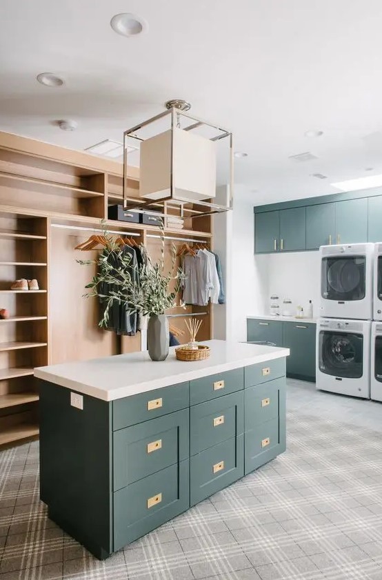 a large modern laundry mudroom with dark green cabinets, white countertops, a light-stained storage unit, a chandelier and washing machines and dryers