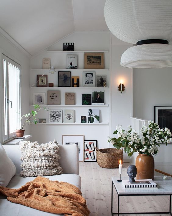 a lovely Scandinavian living room in neutrals with ledges that display art and books, a neutral sofa with a blanket and pillows, some decor
