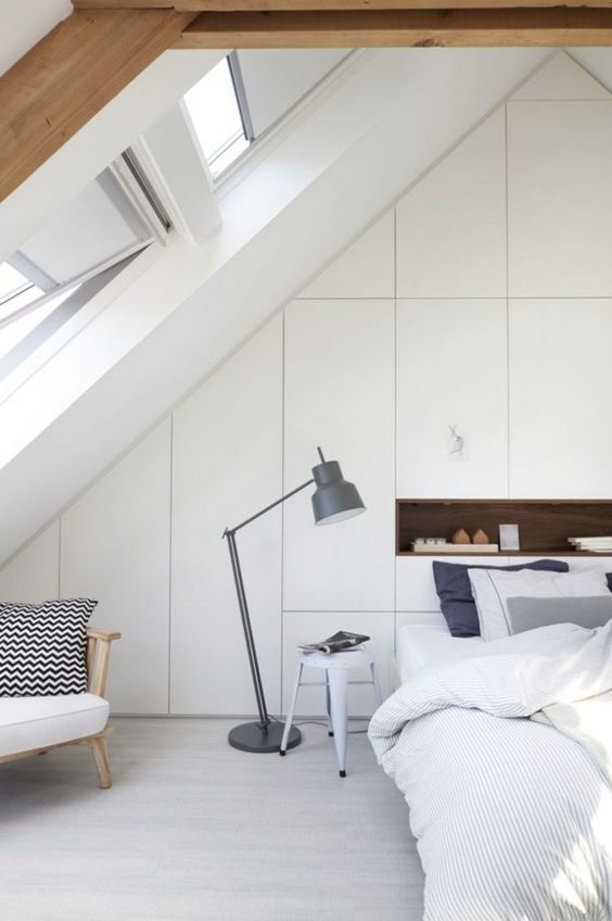 a minimal attic bedroom with a whole built-in storage wall at the headboard, a niche for storage, a bed, a chair and a floor lamp