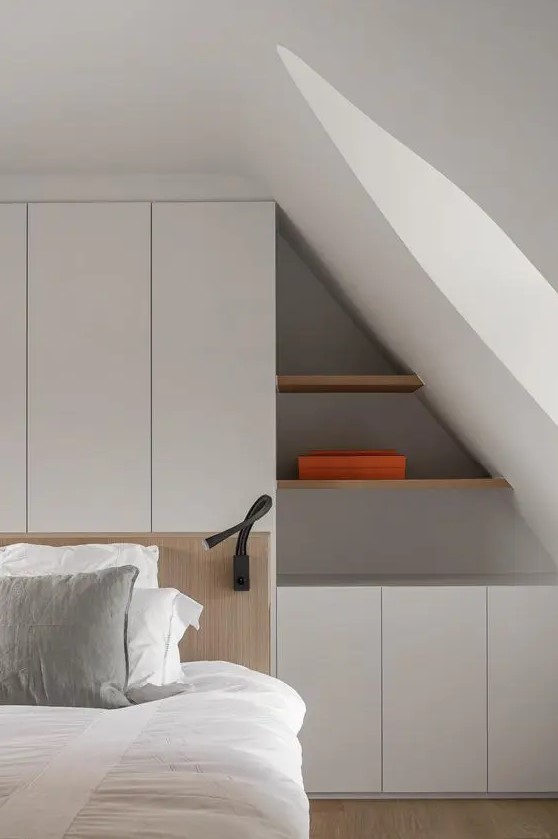 a minimalist attic bedroom with a white storage unit built into the wall, with built-in shelves and cabinets is a smart solution
