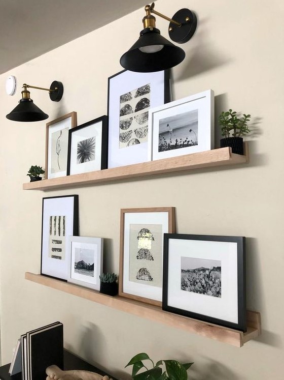 a modern farmhouse gallery wall with light stained wooden ledges, black and white artworks, potted greenery and elegant black sconces