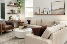 a modern living room with a large neutral sectional, a stained ledge with art, a white coffee table, a brown leather chair and some stained shelves