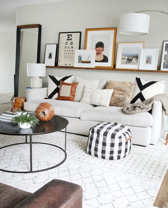a modern living room with a white sofa and printed pillows, a stained ledge with artwork, a black coffee table and some lamps