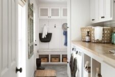 a neutral farmhouse laundry mudroom with shaker cabinets, built-in appliances, a rack and a bench with storage