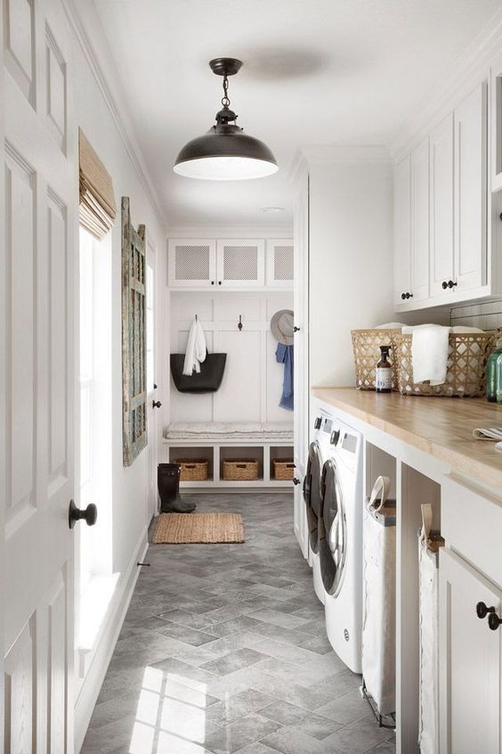 a neutral farmhouse laundry mudroom with shaker cabinets, built-in appliances, a rack and a bench with storage