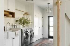 a neutral farmhouse mudroom laundry with built-in cabinets, appliances, a sink, a rug and pendant lamps