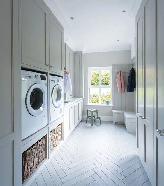 a neutral laundry and mudroom with shaker cabinets, a storage bench, baskets and a washing machine and a dryer