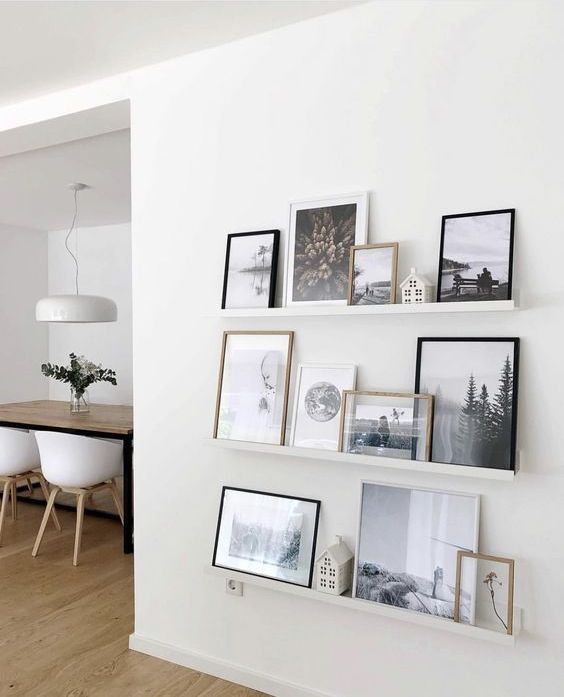a neutral ledge gallery wall with black and white artwork and bright artwork and botanical pieces is a cool idea