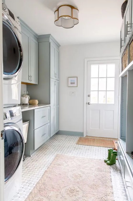 a pale blue mudroom entry with shaker cabinets, an open storage unit with baskets, printed rugs, a washing machine and a dryer