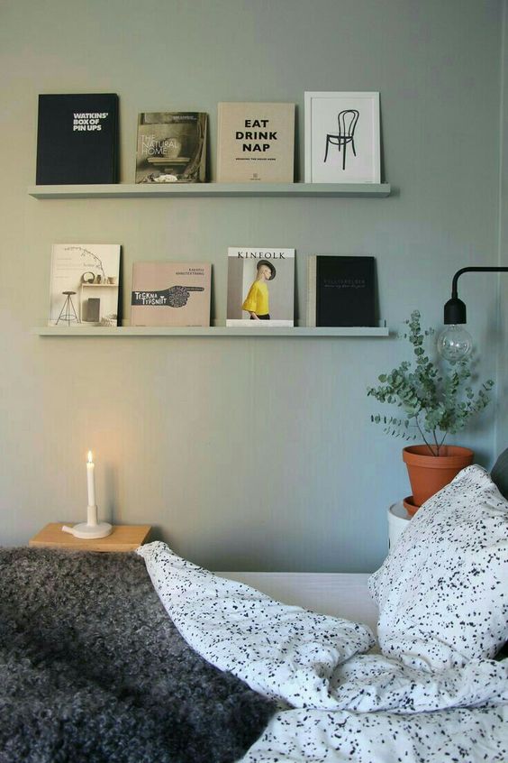 a peaceful bedroom with light green walls and matching ledges that show off books as art, a bed with spotted bedding and some decor