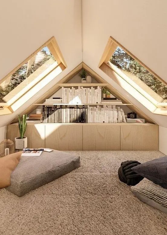 a reading attic space with cabinets, open shelves, cushions and pillows on the floor and skylights that will the space with natural light