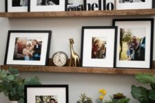 a rustic gallery wall with colorful and black and white artworks in black frames, a clock, a camera and a statuette plus some greenery