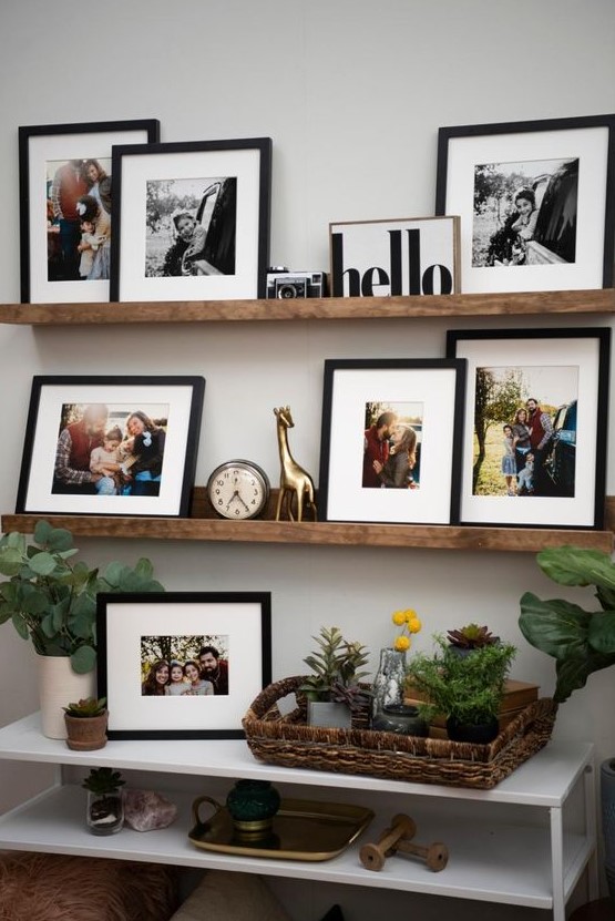 a rustic gallery wall with colorful and black and white artworks in black frames, a clock, a camera and a statuette plus some greenery