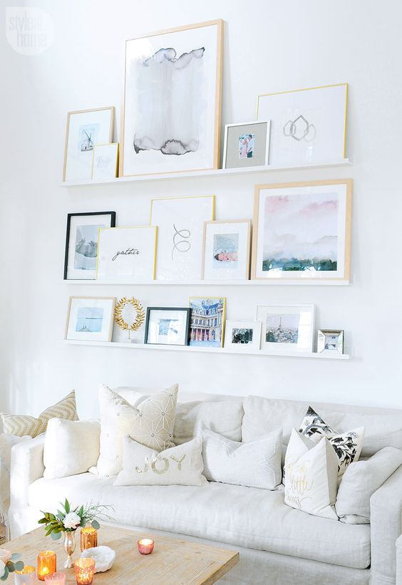 a serene space with a neutral sofa with pillows, a ledge gallery wall with beautiful and airy artwork and a coffee table