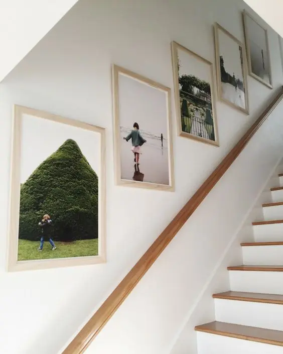 A simple and cool grid gallery wall with family photos in light stained frames is a cool idea for a modern staircase