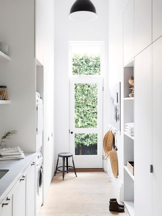 a small and narrow laundry mudroom with open shelves, built-in appliances and a glazed door plus a black pendant lamp