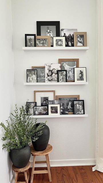 a small lovely nook with short ledges and black and white artworks, wooden stools with black vases and greenery