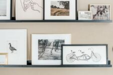 a stylish contemporary gallery wall with black ledges, black and white artworks in blonde wood, white and black frames