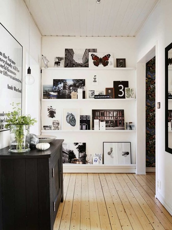a stylish gallery wall with ledges, black and white and colorful artworks, botanical posters and a lamp is very cool