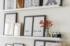 a stylish gallery wall with white ledges, art in black frames, dried blooms in vases, a candle and a vintage camera is a cool idea for a Scandi space