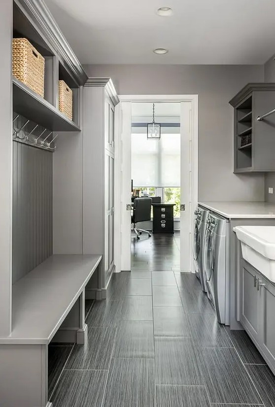 a stylish grey mudroom laundry with an open storage unit and baskets, shaker cabinets, a washing machine and a dryer plus a tile floor