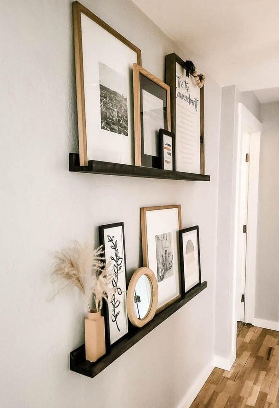 a super chic gallery wall with black ledges, black and white artworks in black and stained frames, pampas grass and wooden beads