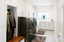 a white mudroom laundry with shaker cabinets, a washing machine and a dryer, a bench with open storage and fluffy rugs