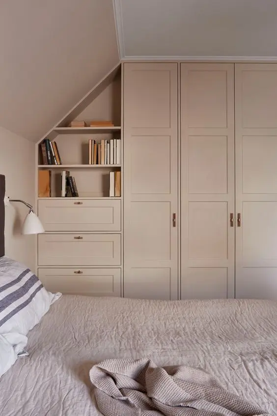 an attic bedroom with a blush accent wall and blush wardrobes and drawers built in is a lovely and welcoming space