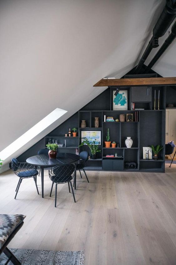 an attic dining room with an attic wall taken by a large storage unit with open compartments, a black table and chairs