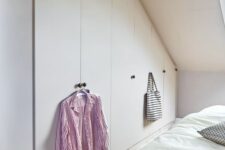 an attic pastel bedroom with built-n wardrobes and a bed, with a skylight is a welcoming space