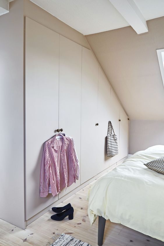 an attic pastel bedroom with built-n wardrobes and a bed, with a skylight is a welcoming space