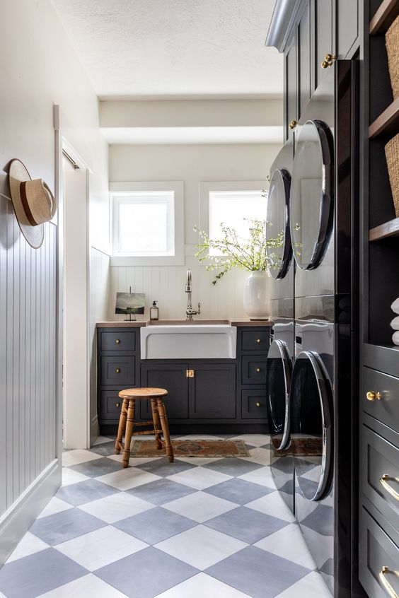 an elegant mudroom laundry with stacked appliances, navy cabinets, a wooden stool and some racks