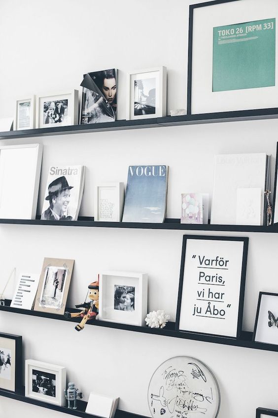 a modern to Scandinavian gallery wall with black ledges, various artwork in black and white frames and books