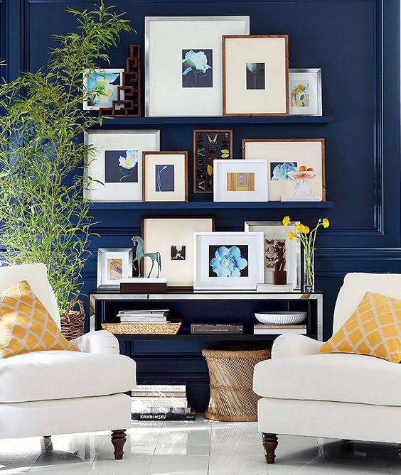 a pretty gallery wall with navy ledges that match walls in color, with colorful and bold artwork in mismatching frames, and with books