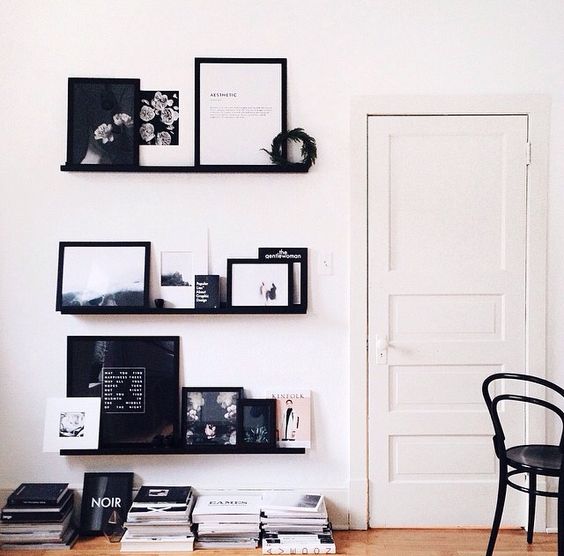 a stylish modern gallery wall with black ledges, black and white artwork in black frames is a cool solution for a modern space