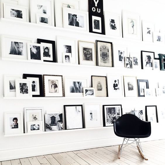 an oversized Scandinavian gallery wall with white ledges and black and white artwork and photos in mismatching frames