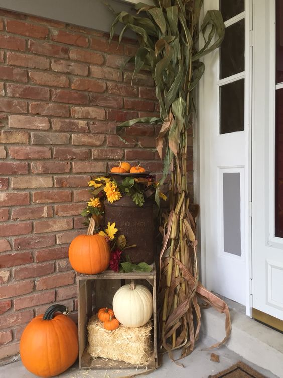 a porch dressed for fall with an old milk can, corn stalks and a crate
