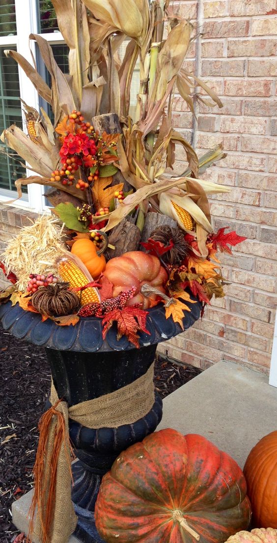 a fall arrangement with corn husks, pumpkins, leaves and hay