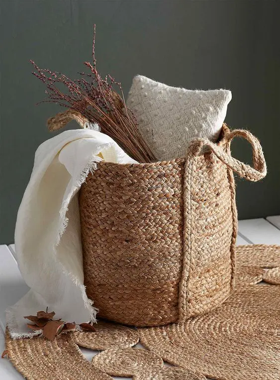a basket with a pillow, a blanket and some dried branches is a cool decor idea for a rustic fall space