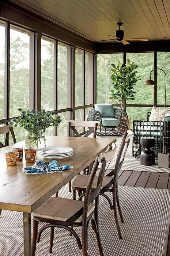 a beautiful neutral screened porch with neutral rugs, a stained dining set, a rattan chair and a sofa, potted plants