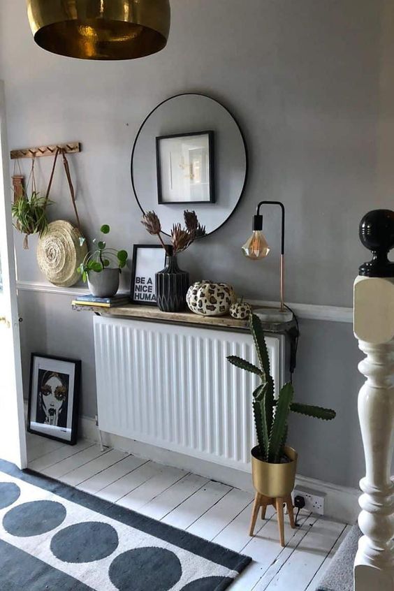 a boho Scandinavian space with a small radiator covered with a shelf with decor and a lamp, a mirror and some plants
