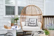 a boho farmhouse patio with a striped rug, a wicker egg-shaped chair, some baskets, potted blooms and a rustic side table with blooms